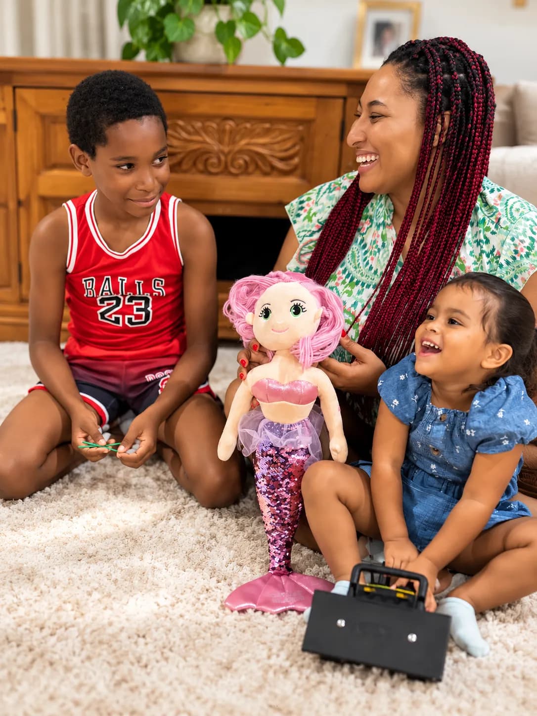 Babysitter playing with a brother and sister and their mermaid doll